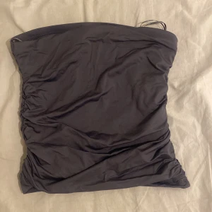 Mörkgrå bandeau tubtopp från Stradivarius - Säljer en mörkgrå bandeau tubtopp från Stradivarius med snygg rynkdetalj framtill. Toppen är axelbandslös och har en tight passform som sitter på plats. Perfekt att styla med jeans eller kjol för en cool look.