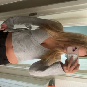 Grå omlottopp med knytband - Snygg grå omlottopp med långa ärmar och knytband i sidan. Toppen är croppad och har en v-ringad halsringning. Perfekt för dig som gillar en enkel men trendig stil. Mjuk och skön, passar till både jeans och kjol.