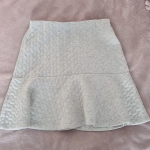 Ljusgrå kjol från Lindex - Supersöt ljusgrå kjol från Lindex i quiltad struktur. Kjolen har en lätt volang nertill som ger en snygg siluett och är i en mjuk, bekväm bomullsblandning. Perfekt för dig som gillar stilrena och trendiga plagg med det lilla extra.