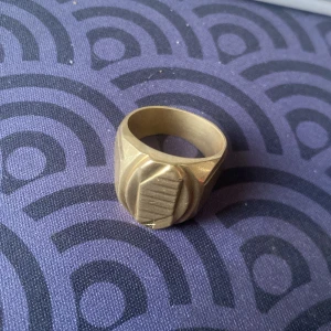 Bred guldring 18K med gravyr - Säljer en bred och tung guldring i 18K med coolt graverat mönster framtill. Ringen väger 18 gram och har en snygg, matt finish. Perfekt statement-piece för dig som gillar unika smycken med lite edge.