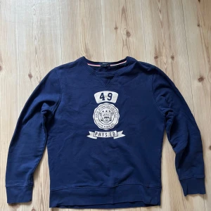 Mörkblå sweatshirt från Gant - Collegeinspirerad mörkblå sweatshirt från Gant med tryck på bröstet som säger 'Five Points College' och 'PHYS.ED'. Tröjan har rund halsringning och långa ärmar. Perfekt för en sportig och avslappnad look.