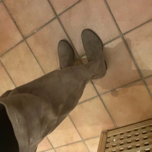 Bruna mocka overknee boots - Säljer ett par snygga overknee boots i brun mocka. Skorna har rund tå och platt sula, perfekt för dig som vill ha en stilren look med lite edge. Passar till både jeans och kjol för en trendig outfit.