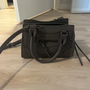 Mörkgrå väska  - Snygg mörkgrå axelväska från Gina, ändats använd ett fåtal gånger, med både handtag och justerbar axelrem. Väskan har flera fack med dragkedja och dekorativa sömmar på sidorna. Perfekt storlek för det viktigaste! NYPRIS 399