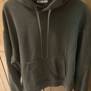 Grön hoodie från Zara med huva - Säljer en grön hoodie från Zara i storlek L. Tröjan har huva med snörning och en stor magficka framtill. Perfekt för dig som gillar en enkel och stilren look. Materialet är mjukt och skönt, passar bra till chill dagar.
