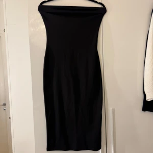Svart axelbandslös klänning - En stilren svart klänning med axelbandslös design och figurnära passform. 