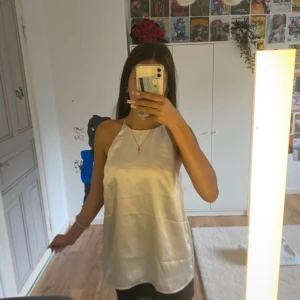 Champagnefärgad satin-klänning H&M - Säljer en stilren champagnefärgad kort klänning från H&M i glansig satin-look. Klänningen är ärmlös med tunna axelband och har en rak, loose passform. Tillverkad av återvunnen polyester, perfekt för dig som gillar minimalistisk och trendig stil.