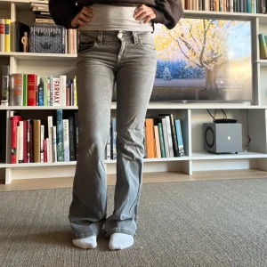 Grå bootcut jeans med lågmidja  - Snygga grå jeans med bootcut passform och lågmidja. Byxorna har coola ficklock bak med knapp och markerade sömmar. Perfekta för dig som gillar en retrovibe och vill ha något som sticker ut lite extra.