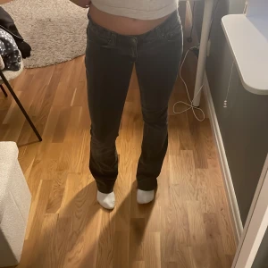 Svarta bootcut jeans med broderad ficka - Säljer ett par svarta jeans med bootcut-modell och låg midja. Jeansen har snygga broderade detaljer på bakfickan och klassisk femficksdesign. Materialet är jeans och passformen är normal. Perfekta för dig som gillar en tidlös look med lite extra edge. Har åxo snören som är innanför byxorna i midjan om midjan e för stor för dig så kan du stjustera de