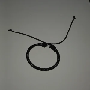 Svart flätat armband med knytband - Stilrent svart armband med flätad design och justerbart knytband. Perfekt accessoar för en enkel men cool look. Passar både tjejer och killar som gillar minimalistiska smycken.