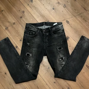 Svarta super skinny jeans Elias Rumelis - Säljer ett par svarta skinny jeans från Elias Rumelis med slitna detaljer och trasiga partier framtill. Jeansen har en tight passform och klassisk femficksdesign. Snyggt tvättade för en cool, lite ruff look.