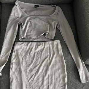 Mörkgrå set  - Säljer en mörkgrå set med en ribbad långkjol med slits på sidan och långarmad topp. Kjolen har en tight passform och hög midja som framhäver figuren. Perfekt att matcha med crop top eller oversized tröja för en trendig look.