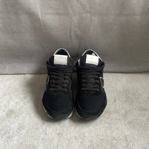 Svarta sneakers från Philippe Model - Snygga svarta sneakers från Philippe Model med vita detaljer och logga på sidan. Skorna har snörning, platt sula och en mix av mocka och syntetmaterial. Perfekta för dig som gillar en sportig och stilren look.Passar 41