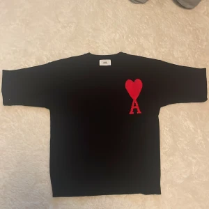 Svart stickad tröja från Ami Paris - Svart stickad tröja från Ami Paris med röd broderad hjärtdetalj och bokstaven A på bröstet. Tröjan har rund halsringning och lång ärm, perfekt för en stilren och trendig look.