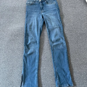 Blå Molly jeans från Gina Tricot - Snygga blå Molly jeans från Gina Tricot med klassisk femficksdesign och slits nertill på benen. Jeansen har hög midja och raka ben med en lätt utsvängd bootcut-stil. Tillverkade i bomull med en skön stretch. Perfekta för dig som gillar en tidlös look.
