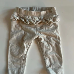 Beige leggings med volang från Newbie - Supersöta beige leggings från Newbie i mjuk bomullskvalitet. De har en elastisk midja och en gullig volangdetalj upptill som ger extra charm. Perfekta för små barn som vill ha något bekvämt och stilrent.