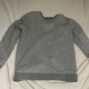 Grå sweatshirt från Gant - Klassisk grå sweatshirt från Gant med rund halsringning och diskret logga på bröstet. Tröjan har ribbade muddar vid ärmslut och nederkant, perfekt för en clean och stilren look. Tillverkad i mjuk bomull för maximal komfort.