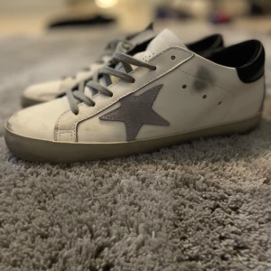 Golden Goose skor  - Golden Goose sneakers i vitt skinn med grå mockadetaljer och ikonisk stjärna på sidan. Skick 9/10, Ingen box tyvärr och pris kan diskuteras. Svarar ändast seriösa köpare‼️