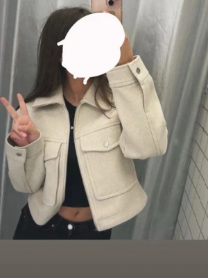 Beige overshirt med fickor och dragkedja - Bershka kappa. Snygg beige overshirt med stora bröstfickor och dragkedja framtill. Jackan har en croppad passform, klassisk krage och långa ärmar med knappdetaljer vid mudden. Perfekt för lager-på-lager och enkel att styla till olika outfits.