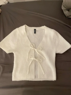 Vit ribbad croppad topp med knyt - Vit ribbad topp från h&m. Den sticks inte utan är i mjukt material. Storlek xs och har inga töcken på användning.