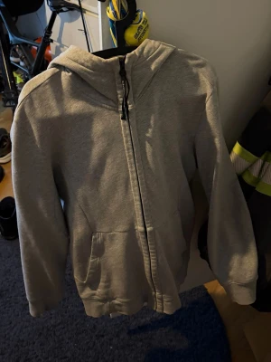 Grå hoodie med glasögon i huvan - Säljer en grå zip-hoodie från C.P. Company med deras ikoniska glasögon i huvan. Hoodien har dragkedja framtill, två fickor och är tillverkad i mjukt bomullsmaterial. Perfekt för dig som vill sticka ut med en unik streetwear-look.