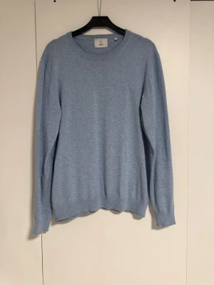 Ljusblå stickad tröja från Bläck - Ljusblå stickad tröja från Bläck med rund halsringning och ribbade muddar vid ärmslut och nederkant. Enkel och stilren design som passar perfekt till jeans eller chinos.