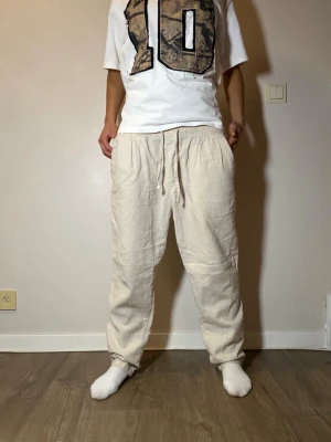 Beiga linnebyxor med snörning - Säljer ett par beiga linnebyxor med avslappnad passform och dragsko i midjan. Byxorna har raka ben och sidofickor, perfekta för en chill och stilren look. Materialet är luftigt linne som passar grymt till varmare dagar.