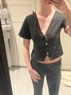 Svart v-ringad topp från 157 - Svart kortärmad topp från 157 med v-ringning och knappar framtill. Modellen är croppad och har en enkel, stilren design som passar till mycket. Perfekt för dig som gillar en clean och modern look. Pris diskuteras gärna! 