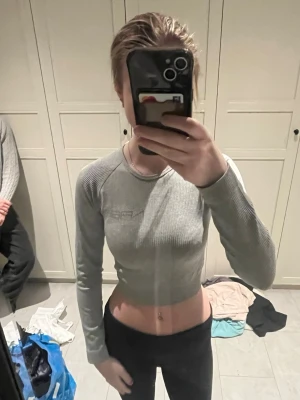 Grå croppad tränings topp från New Apparel - Snygg grå croppad långärmad tränings topp från New Apparel. Toppen är ribbad och har en tight passform med rund halsringning. Pris diskuteras gärna! 