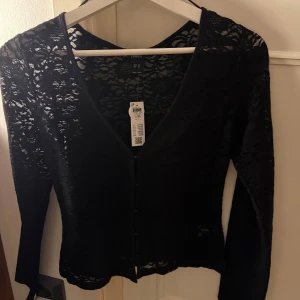 Spets topp - Säljer en superfin svart spetstopp från Lindex med långa ärmar och knäppning framtill. Toppen har v-ringning