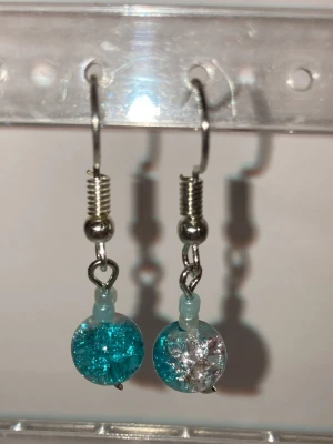 Turkosa och genomskinliga glashängen - Handgjorda unika örhängen med runda hängen i turkost och genomskinligt glas. Hängena har en sprucken effekt som ger ett coolt och glittrande intryck. Krokarna är i metall med spiralformad detalj upptill. Perfekta för dig som gillar färg och vill sticka ut. Kontakta mig vid frågor eller vid köp.