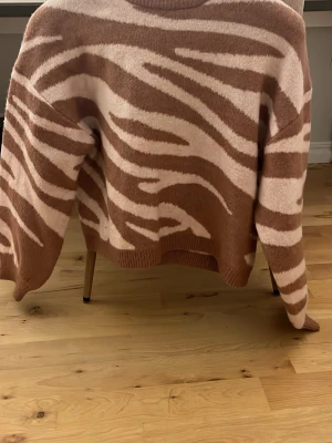 Stickad tröja med zebramönster - Cool stickad tröja i brunt och ljusrosa med zebrainspirerat mönster. Tröjan har rund halsringning, långa ärmar och ribbade muddar. Perfekt för dig som gillar djurmönster och vill sticka ut lite extra.