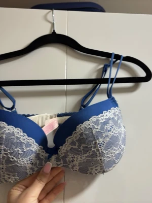 Blå push-up bh med spetsdetaljer - Snygg blå push-up bh med vita spetsdetaljer över kuporna och dubbla axelband för en trendig look. Bh:n har vadderade kupor och hakknäppning bak. sopass elegant och feminin design, perfekt för dig som gillar fina detaljer.