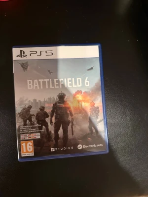 Battlefield 6 till PS5 - Battlefield 6 till PlayStation 5, ett actionfyllt FPS-spel från Electronic Arts. Omslaget är blått med militärtema och explosioner i bakgrunden. Perfekt för dig som gillar intensiva strider och multiplayer.