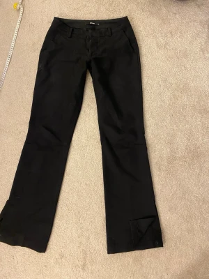 Svarta kostymbyxor bootcut - Snygga svarta kostymbyxor med bootcut passform och klassiska fickor fram. Byxorna har bälteshällor och stängs med dragkedja och knapp. Perfekta för en clean och stilren look. De är ett litet hål i ena fickan i fram men som lätta skulle kunna sys eller limmas ihop 
