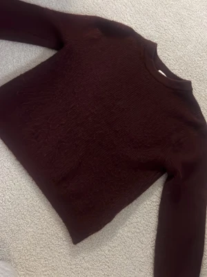 Mörkröd stickad tröja - En enkel och stilren mörkröd stickad tröja med rund halsringning och långa ärmar. Perfekt för lager-på-lager och passar till många olika outfits.