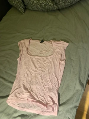 Ljusrosa topp från Gina Tricot - En ljusrosa topp från Gina Tricot med rund halsringning och korta ärmar. Tunt och mjukt material som känns skönt mot huden. Perfekt att matcha med jeans eller kjol för en enkel och snygg look. Bara andvända 1 gång 