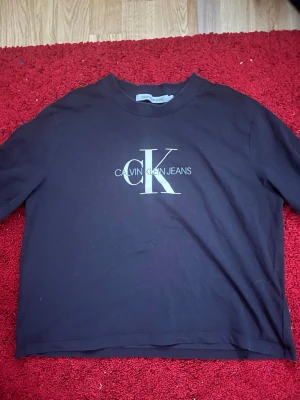 Svart Calvin Klein Jeans t-shirt - Snygg svart t-shirt från Calvin Klein Jeans med stort vitt CK-logotryck på bröstet. Klassisk rund hals och korta ärmar. Tillverkad i mjuk bomull för en bekväm känsla och enkel att matcha till olika outfits.