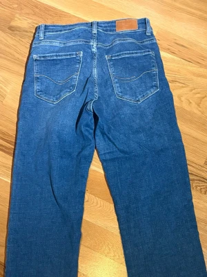 Blå raka jeans med klassisk passform - Snygga blå jeans med en klassisk femficksdesign och lite utsvängda ben. Jeansen har normal passform och är tillverkade i ett mjukt denimtyg. Perfekta för en avslappnad och stilren look.