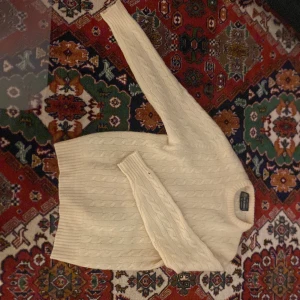 Vit kabelstickad ulltröja - Kabelstickad vit tröja i 100% ren lammull från Handknit Import. Tröjan har rund halsringning och klassiskt mönster, perfekt för kalla dagar. Snygg och tidlös design som passar till många olika stilar.