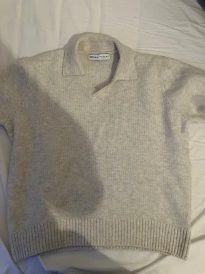 Beige stickad tröja från Bershka - Säljer en beige stickad tröja från Bershka med krage och v-ringning. Tröjan har långa ärmar och ribbade muddar vid ärmslut och nederkant. Perfekt för lager på lager och enkel att matcha till olika outfits.