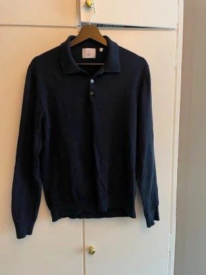 Mörkblå långärmad piké från Boos - Klassisk mörkblå långärmad piké från Bläck med krage och knappar framtill. Tillverkad i merinoull och passar perfekt till jeans eller chinos för en clean och stilren look. Sparsamt använd utan några hål eller skador. Tvecka inte på att höra dig om du har någon fråga.