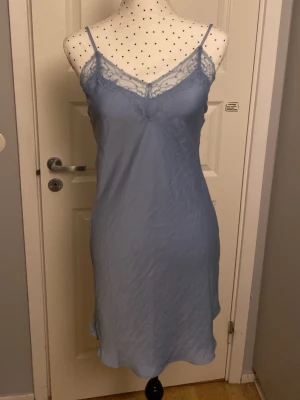 Ljusblått nattlinne med spetsdetaljer - Säljer ett ljusblått nattlinne med tunna axelband och vacker spets vid urringningen. Nattlinnet har en mjuk och följsam passform som känns skön mot huden. Perfekt för mysiga kvällar hemma.
