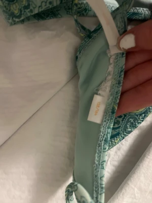 Grön paisleymönstrad bikini från OYSHO - Snygg bikini från Gina tricot i grönt med paisleymönster och justerbara axelband. Bikinin har en klassisk bygelmodell och spänne i ryggen. Perfekt för strand eller poolhäng. Materialet är mjukt och följsamt för bästa komfort.