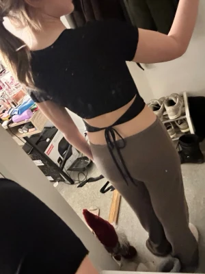 Svart croppad topp med snörning - Svart croppad topp med korta ärmar och snygg snörning i ryggen som knyts. Perfekt för dig som gillar trendiga och stilrena plagg. Toppen har en tight passform och är tillverkad i ett mjukt, stretchigt material.