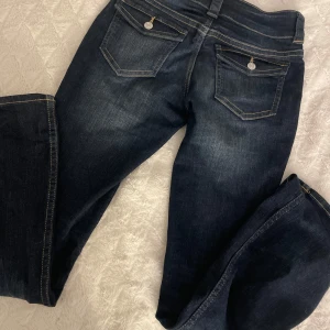 Mörkblå jeans med bootcut - Snygga mörkblå jeans med bootcut och klassiska kontrastsömmar. Jeansen har dubbla knappar i midjan, fem fickor och coola detaljer med ficklock och silverfärgade knappar bak. Storlek 170 men passar xs/s💕 pris kan diskuteras men de är aldrig använda! Nypris 350 tror ja☺️