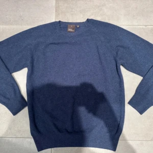 Blå tröja från Oscar Jacobson - Ej använd blå stickad tröja från Oscar Jacobson med rund hals och långa ärmar. Perfekt för dig som gillar stilrena och klassiska plagg. Mjuk och skön kvalitet. Nypris 1300 