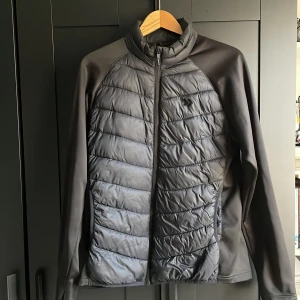 Svart quiltad pufferjacka - Snygg svart pufferjacka från Swedemount med quiltad framsida och rygg. Jackan har hel dragkedja, hög krage och släta ärmar i stretchigt material. Perfekt för dig som vill ha en sportig och stilren look.