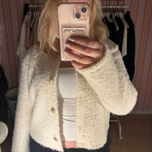 Vit fluffig kofta med guldknappar - Superfin vit kofta med fluffig, mjuk känsla och tre snygga guldknappar framtill. Koftan har lång ärm och en lite boxig, croppad passform. Från Hm i stl. L