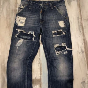 Blå slitna jeans med hål - Riktigt snygga blå jeans med rejält slitna detaljer och stora hål på både fram- och baksida. Jeansen har klassisk femficksmodell och cool tvättad look. Perfekta för dig som gillar en edgy och avslappnad stil 