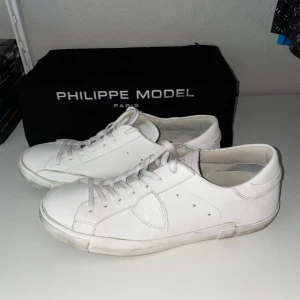 Vita Philippe Model sneakers i skinn - Snygga vita sneakers från Philippe Model Paris i stilren design. Originallåda medkommer. Endast använda enstaka gång, köpta från MerchSweden. Storlek 43. 